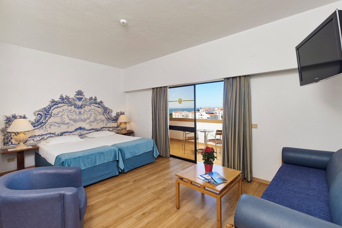 Habitación de hotel con cama, sofá, mesa, televisión y vista a la ciudad.