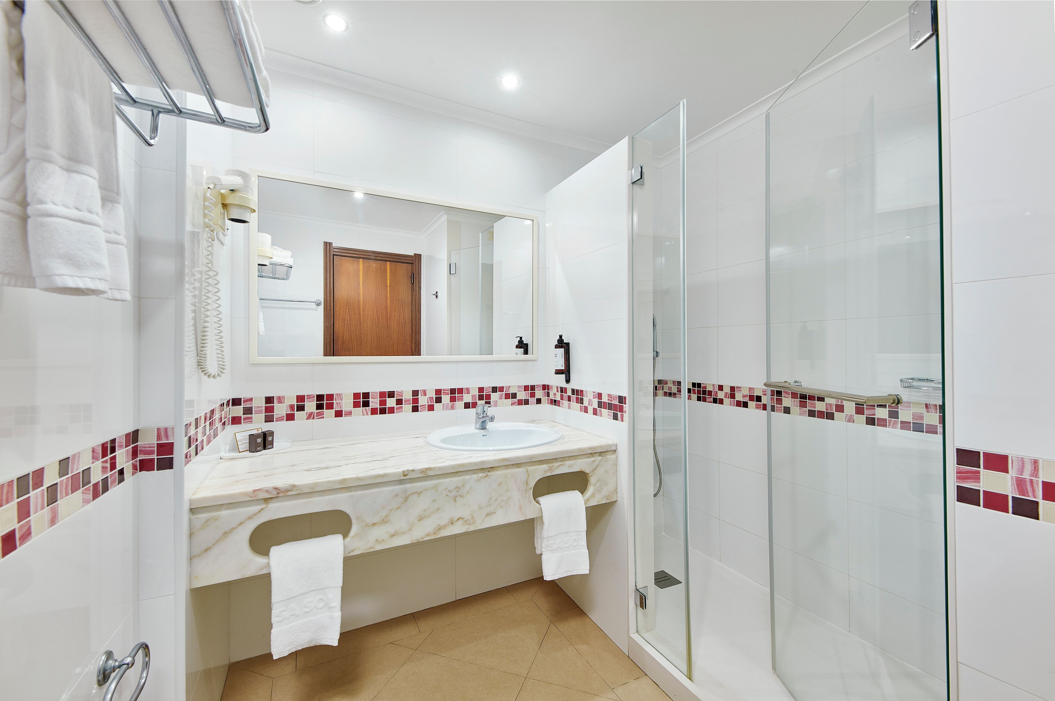 A modern bathroom with a marble sink, a glass shower enclosure, and a mirror with a wooden door in the background.