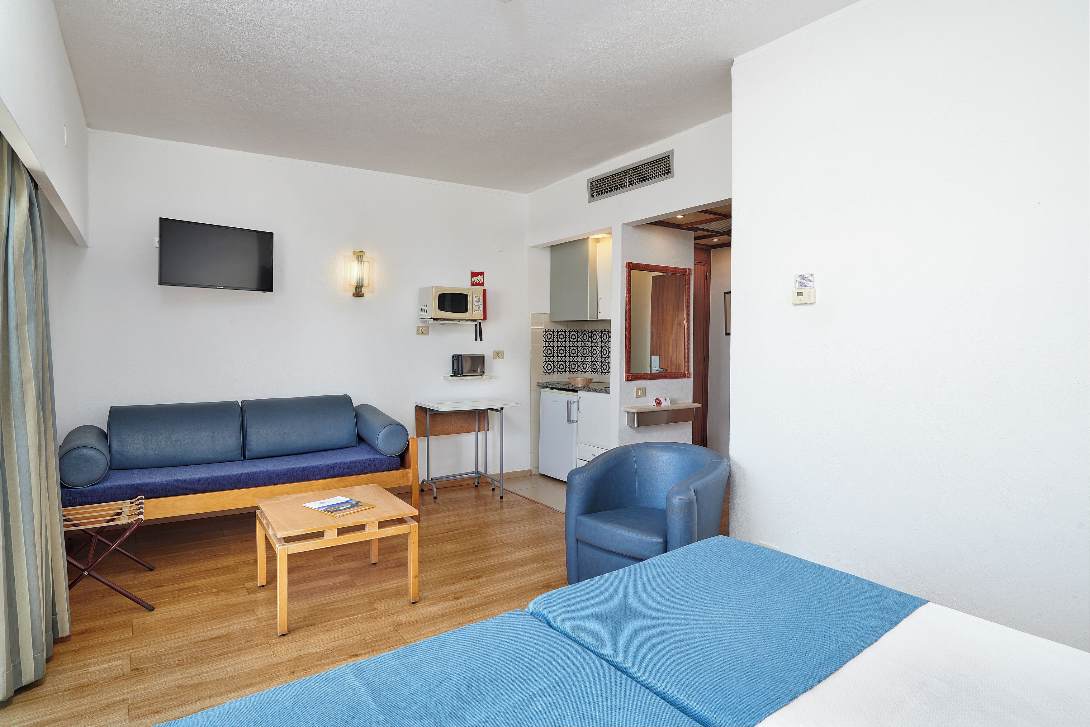 Espaço compacto para viver, com sofá, mesinha, cadeira, cama, televisão, micro-ondas e kitchenette.