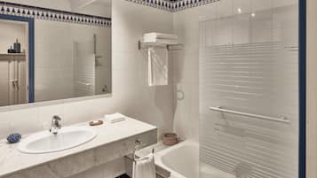A bathroom with a white sink, mirror, and bathtub. There is a towel rack with towels and a basket.