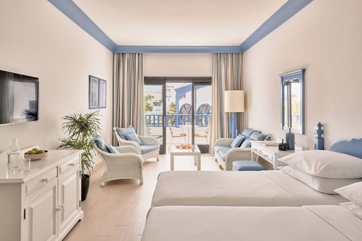 Een moderne hotelkamer met een groot bed, een bureau, een stoel, een kamerplant en een balkon met uitzicht.