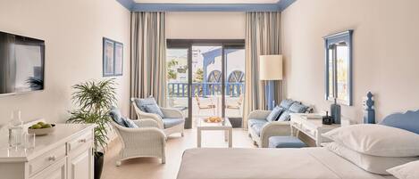 Een hotelkamer met een bed, twee stoelen, een bureau, een televisie, een plant en een balkon met uitzicht.