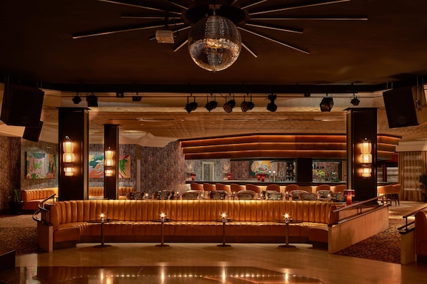 A modern bar area with a curved seating arrangement, overhead lighting, and a disco ball.