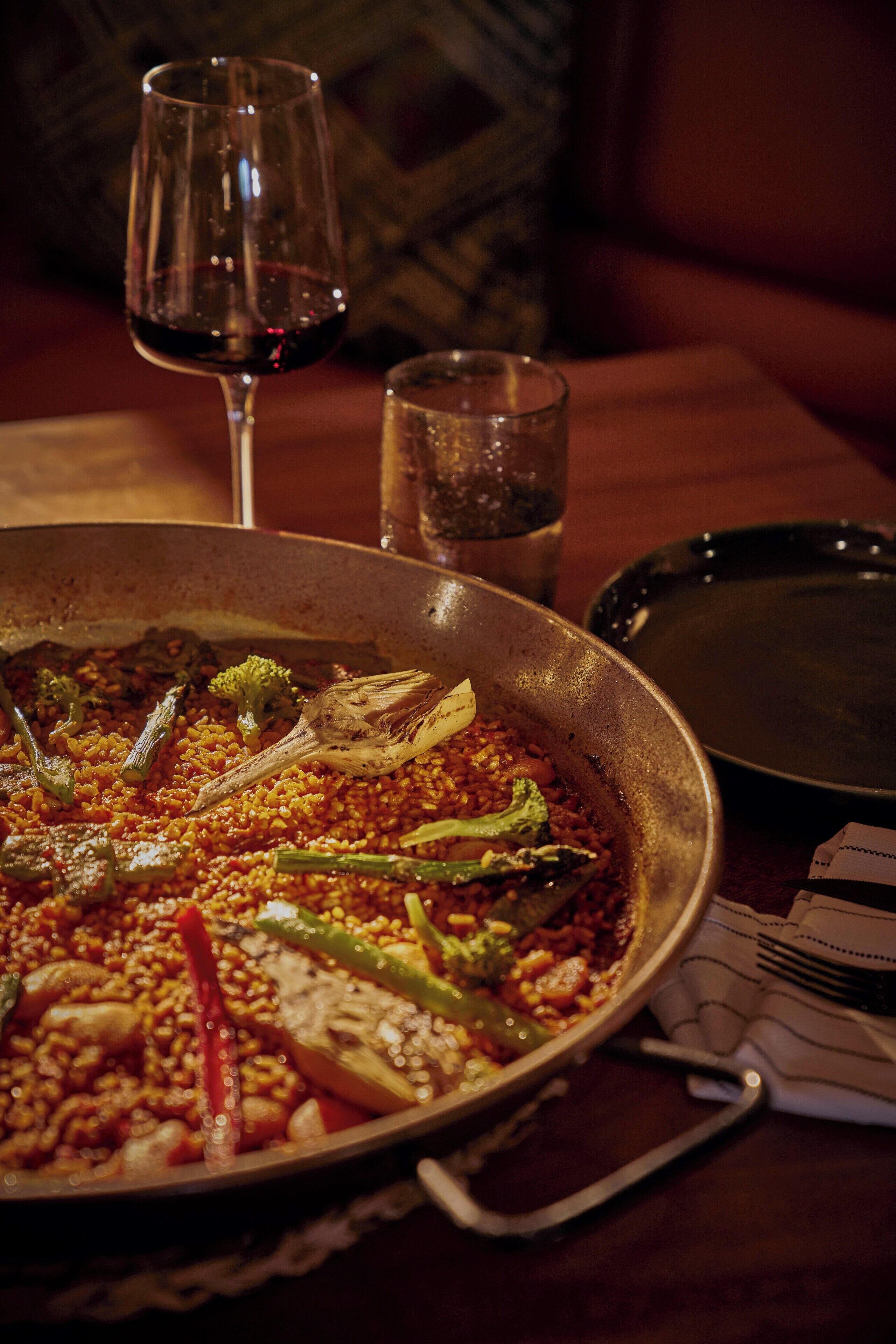 A dining table with a pan of food, a glass of red wine, and a glass of water.