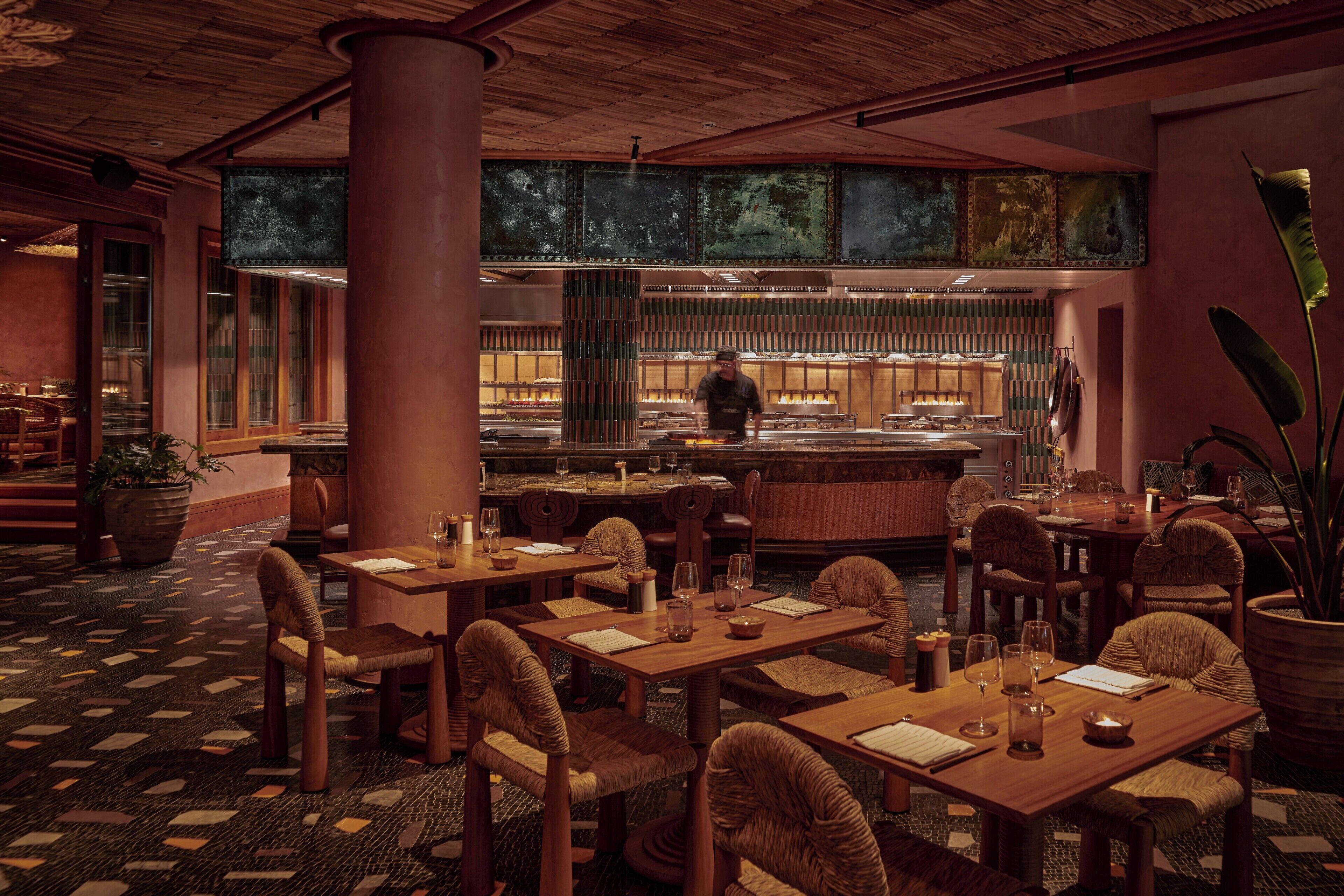 A restaurant with wooden tables and chairs, a chef at the counter, and a patterned floor.