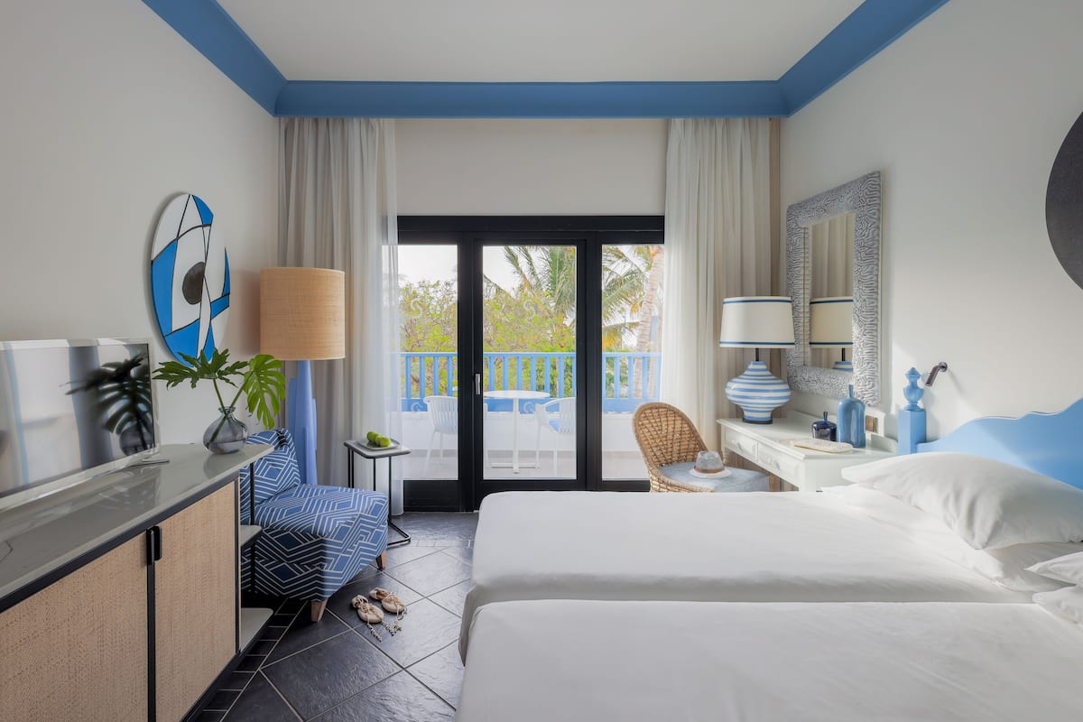 Een hotelkamer met een bed, een bureau, een stoel, een lamp en uitzicht op het balkon.