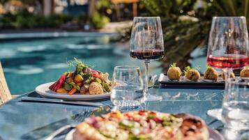 Mesa de comedor con comida, copas de vino y ambiente junto a la piscina.