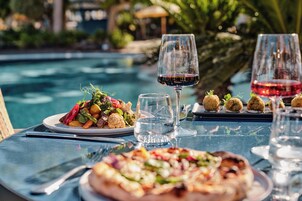 Mesa de comedor con comida, copas de vino y ambiente junto a la piscina.