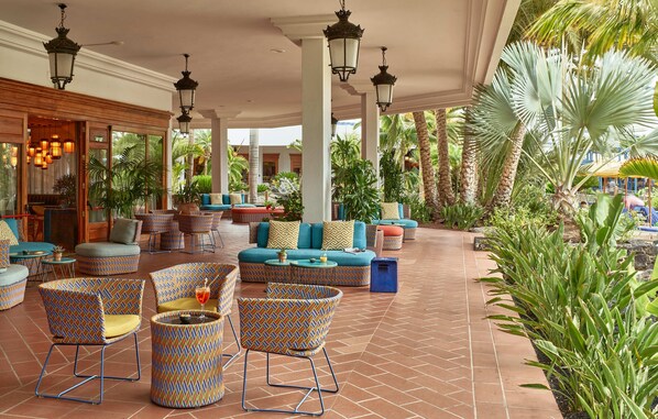 A spacious outdoor lounge area with patterned furniture, large windows, and a variety of plants. - Seaside Los Jameos (Tías)