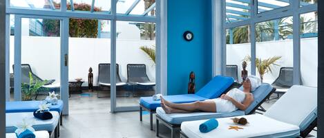 A spa area with reclining chairs, a massage table, and a large window with a view of palm trees.