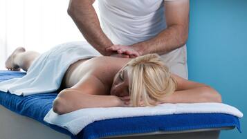 Une séance de massage dans une pièce dont un mur est bleu et qui contient une étagère en bois ornée d’objets décoratifs.