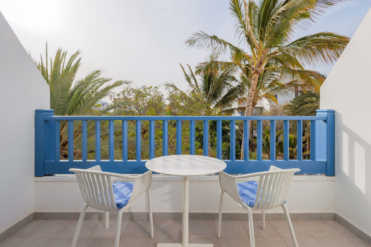 Een balkon met een witte tafel en twee witte stoelen, blauwe kussens en een blauwe balustrade.