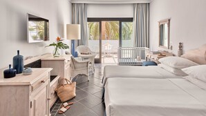 A hotel room with two beds, a desk, a chair, a crib, and a balcony with a view of palm trees. - Seaside Los Jameos (Tías)