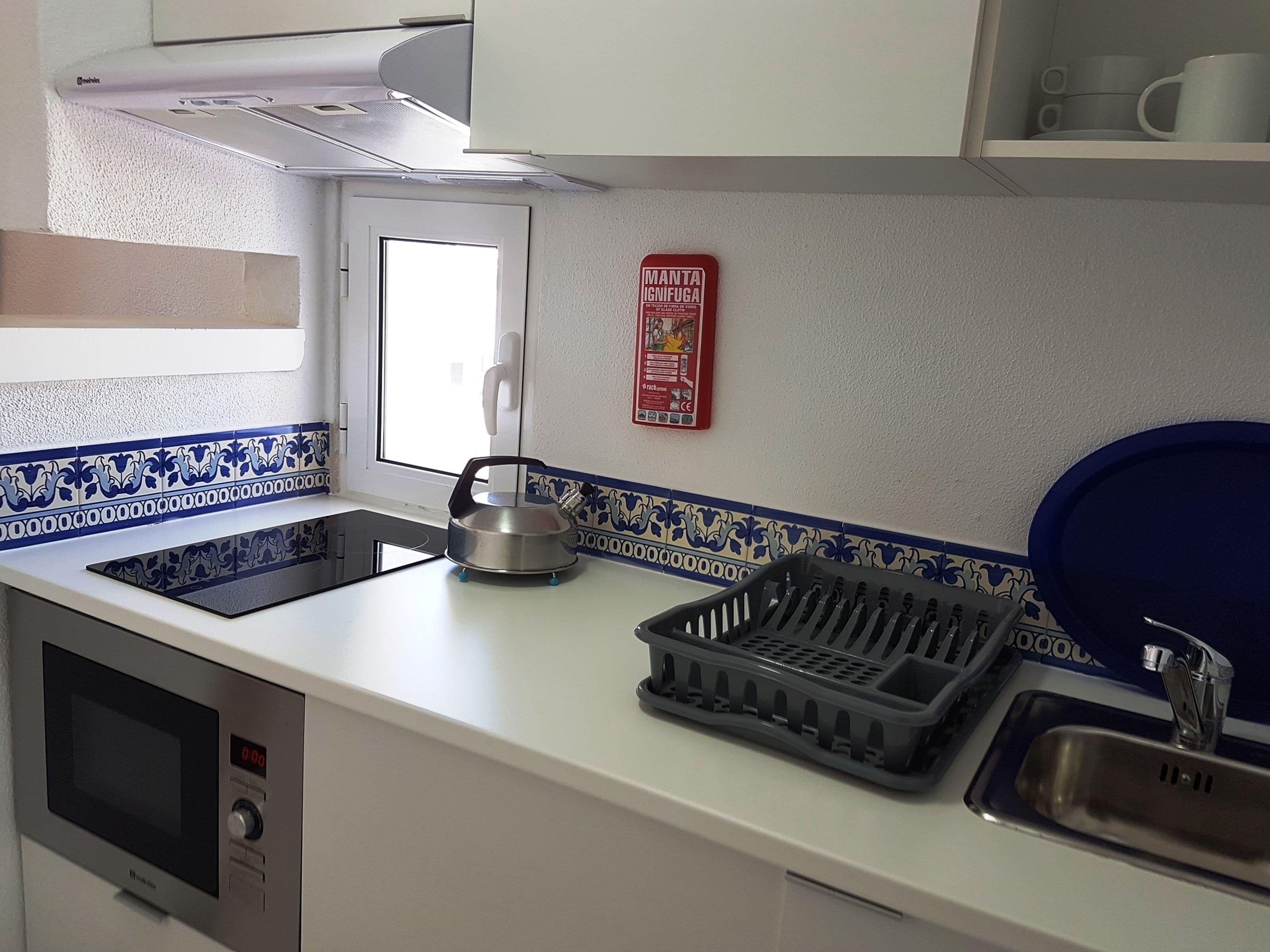 Een keuken met een magnetron, waterkoker, spoelbak en een afdruiprek.