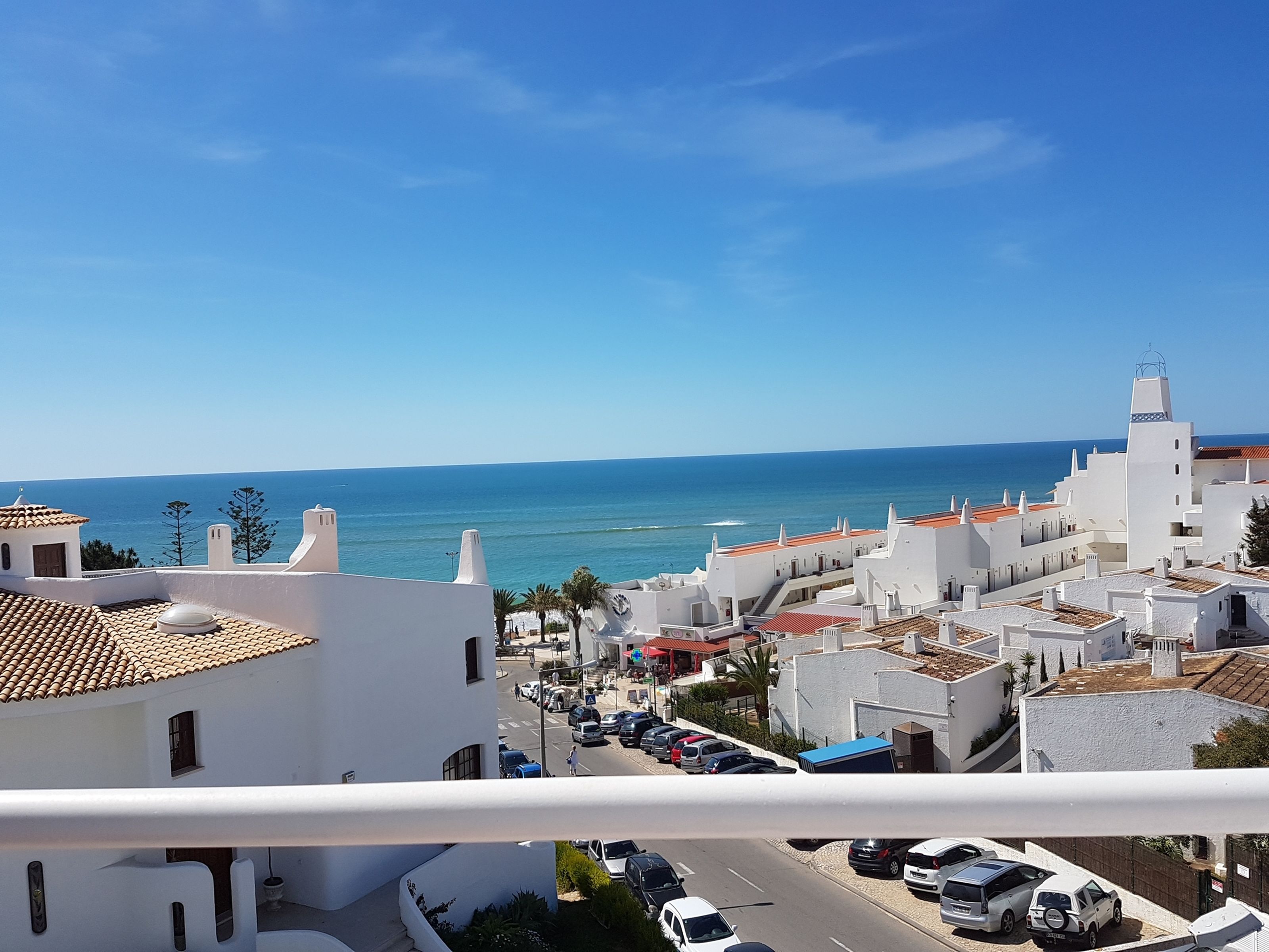 A coastal town with white buildings, a clear blue sky, and the sea in the background.