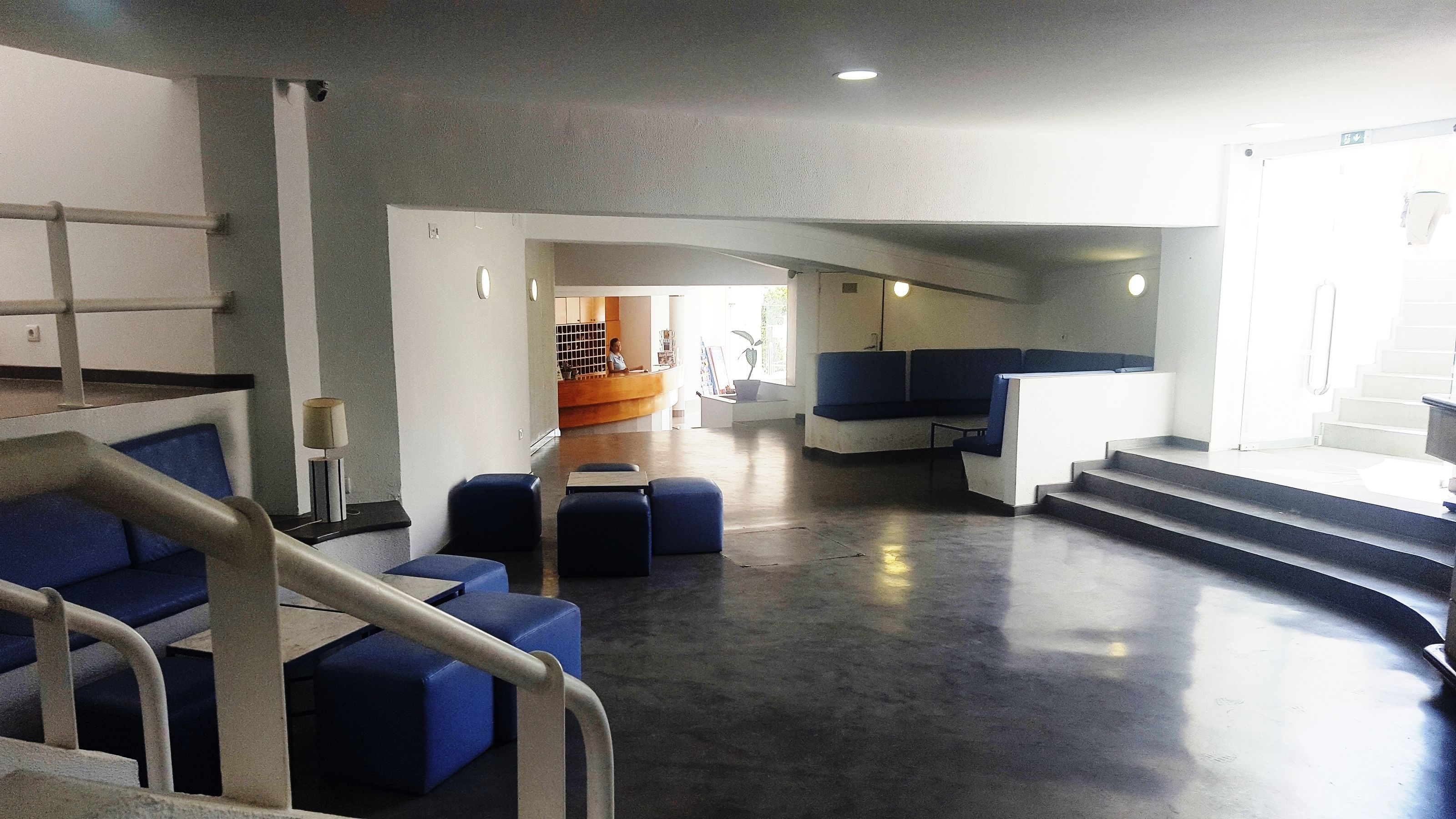 A spacious lobby with a curved staircase, blue seating areas, and a reception desk.