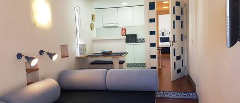 Una sala de estar moderna con un sofá, un comedor con mesa y sillas, y una cocina al fondo.