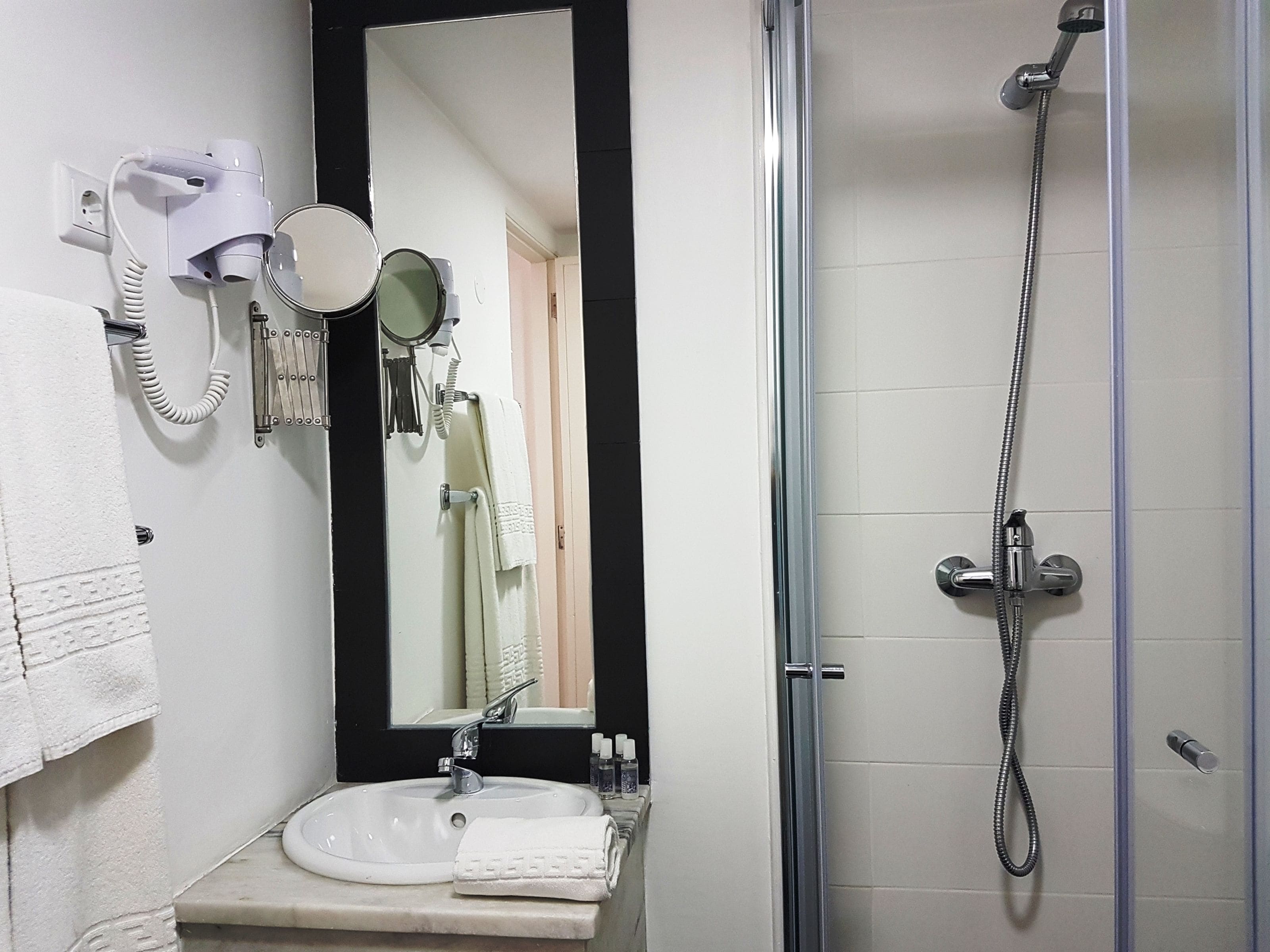 A bathroom with a sink, mirror, hairdryer, and shower.