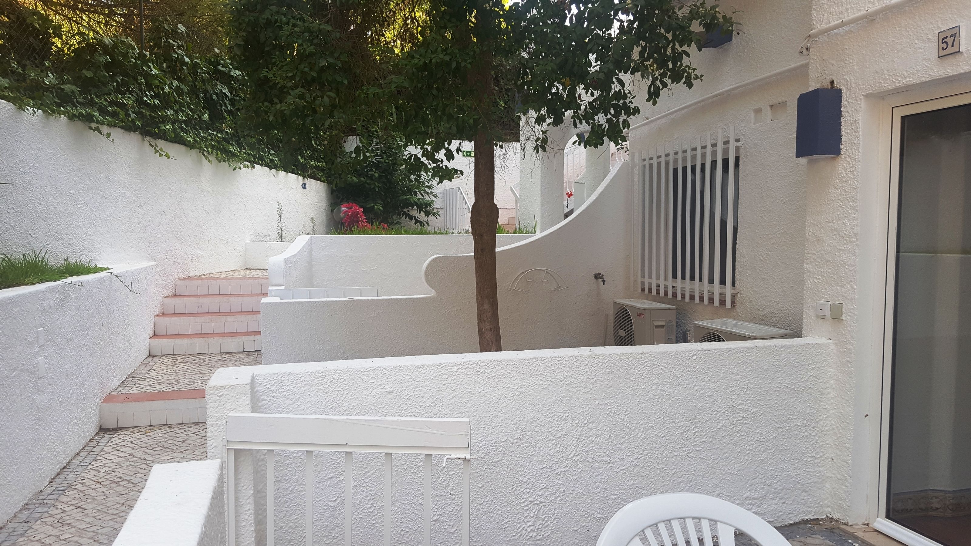 A white-walled courtyard with a tree, a small staircase, and a window with bars.