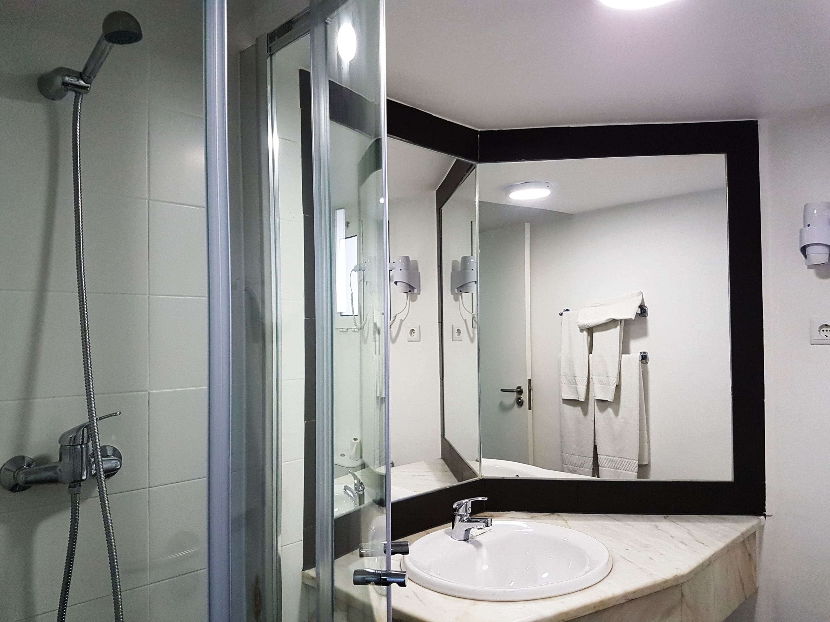 Un baño moderno con ducha de vidrio, lavabo blanco y un espejo grande.
