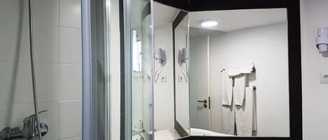 Un baño moderno con ducha de vidrio, lavabo blanco y un espejo grande.