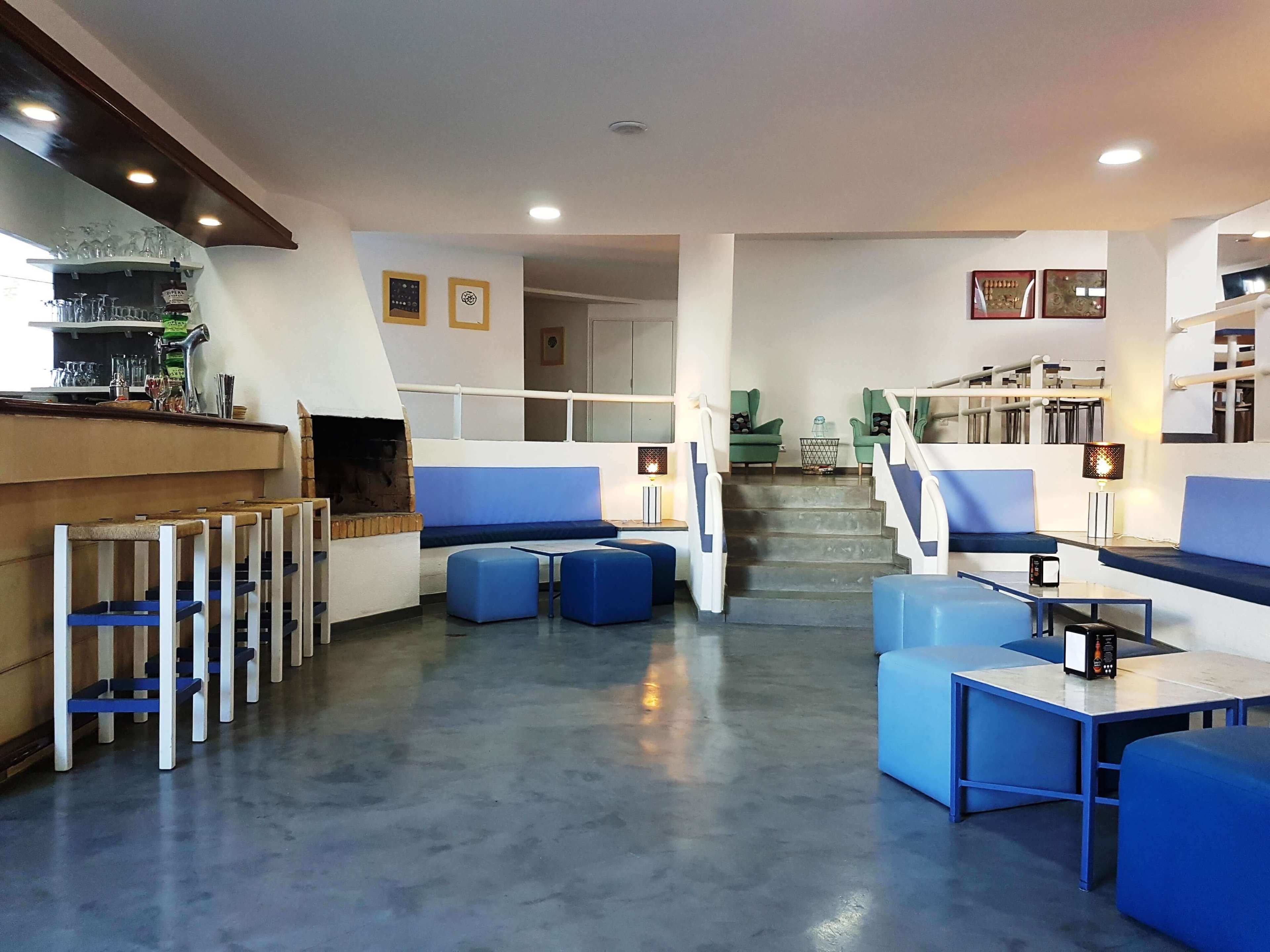 Un espace de détente moderne avec des sièges bleus, un bar et un escalier menant à un autre niveau.