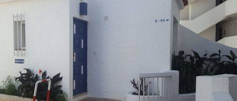 A white building with a blue door, numbered 29, and a small garden area with plants.