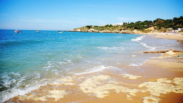 A beach with clear blue water, a sandy shore, and a rocky hillside in the background. - Apartamentos Soldoiro (Albufeira)