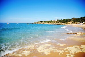 A beach with clear blue water, a sandy shore, and a rocky hillside in the background. - Apartamentos Soldoiro (Albufeira)