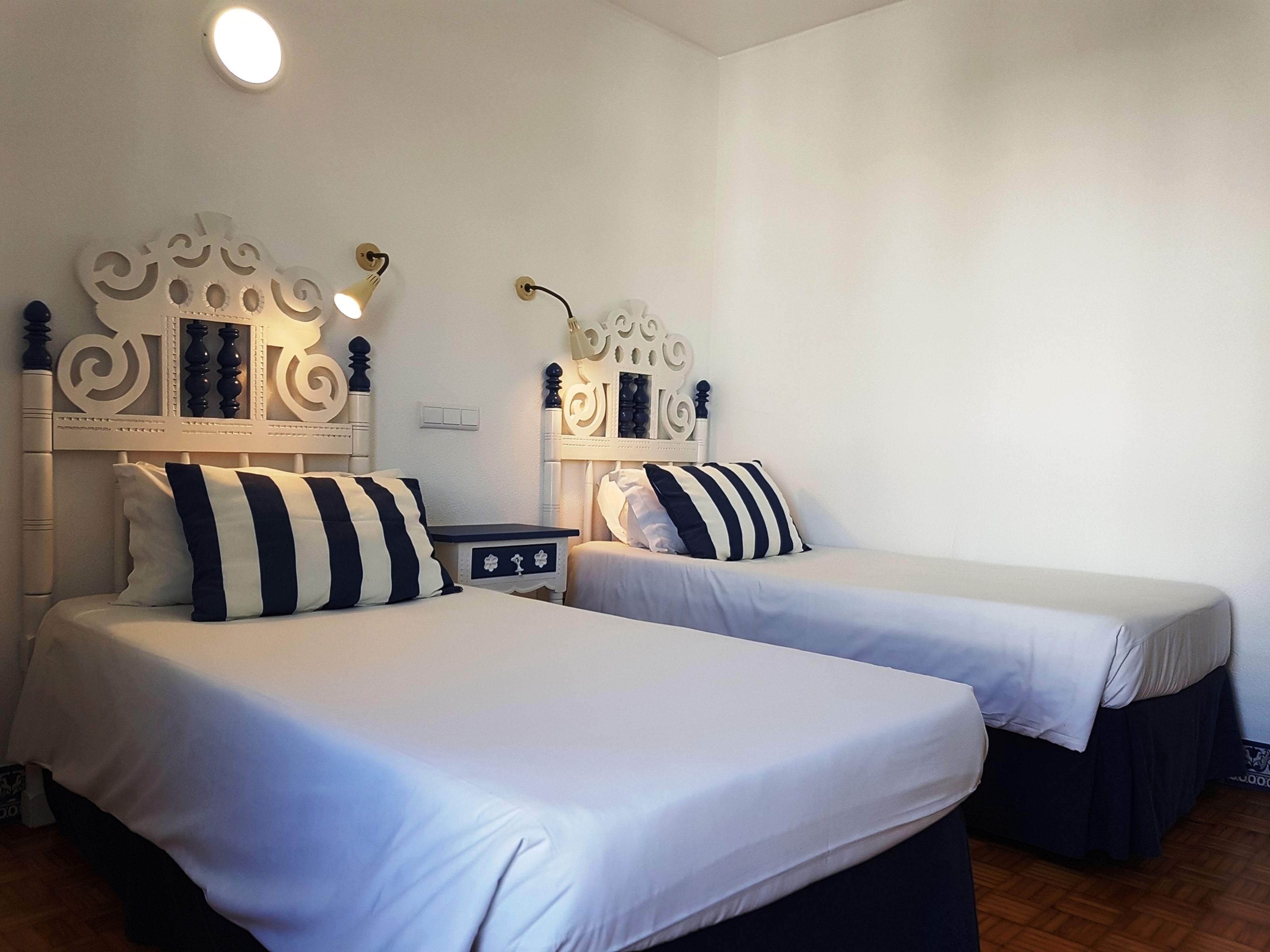 Ein Hotelzimmer mit zwei Betten, jeweils mit einem verzierten Kopfteil und gestreiften Kissen.