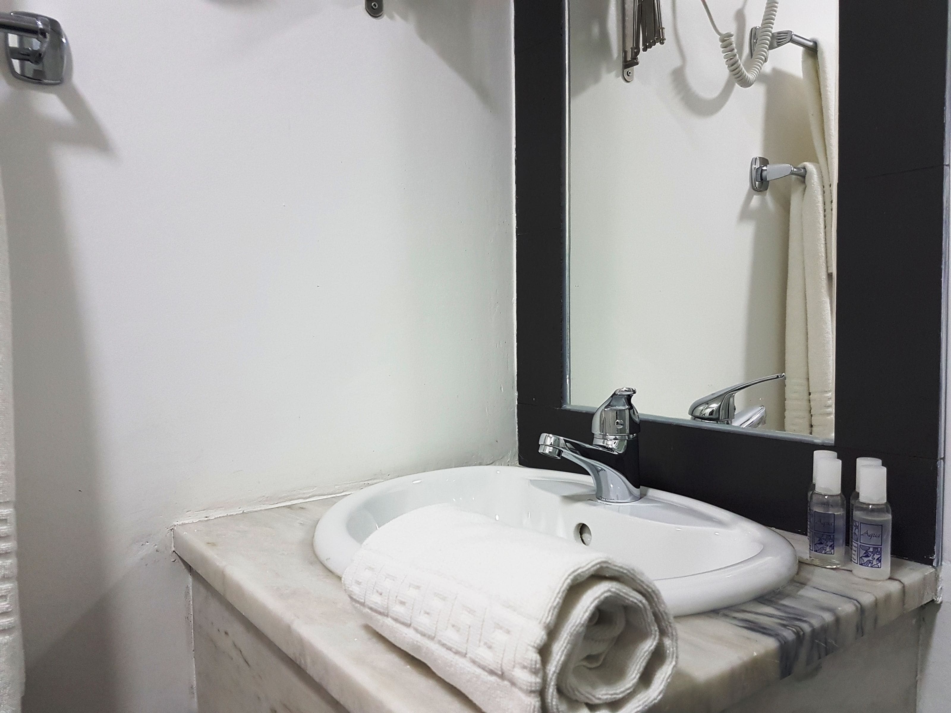 Un baño con un lavamanos blanco, un espejo y una toalla en la encimera.