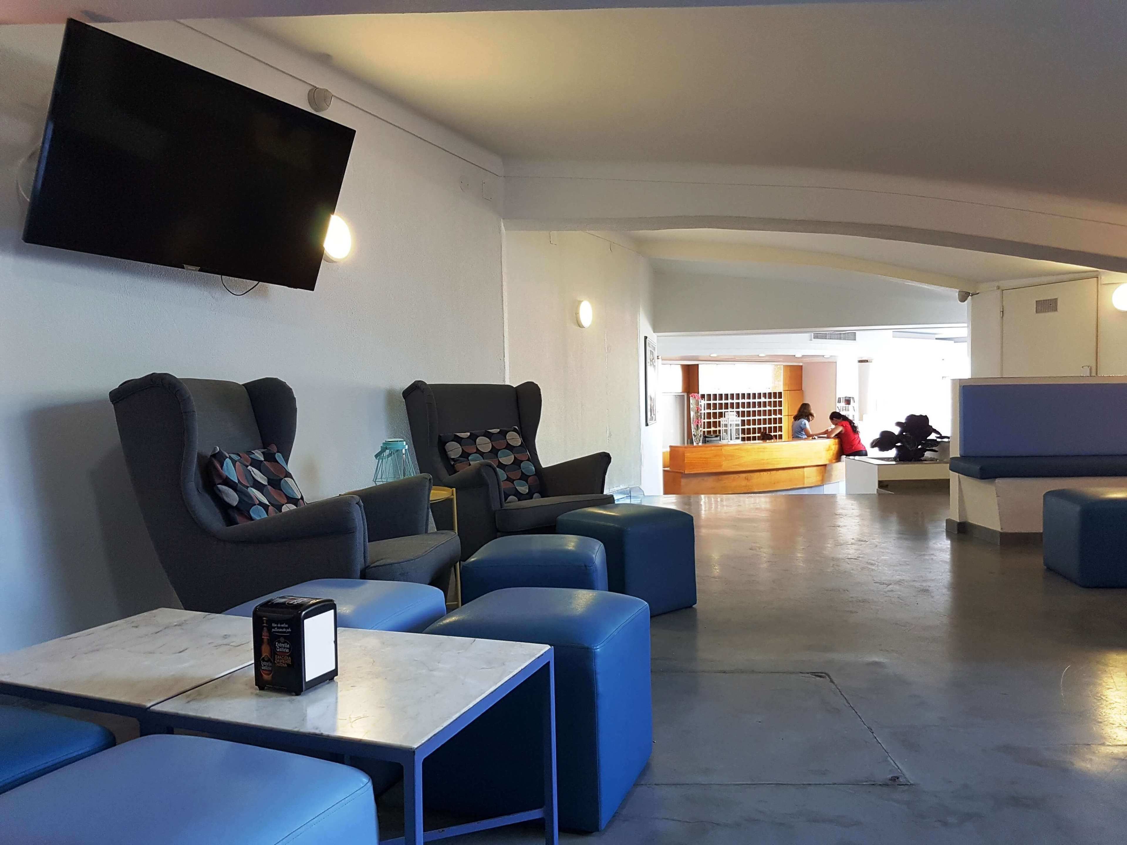 A modern lounge area with comfortable seating, a flat-screen TV, and a reception desk in the background.