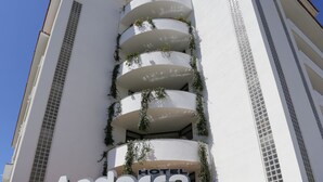 Ein Hotel namens Andorra mit modernem Design, das einen markanten Eingang, mehrere mit Pflanzen bepflanzte Balkone und einen klaren, blauen Himmel im Hintergrund zeigt.