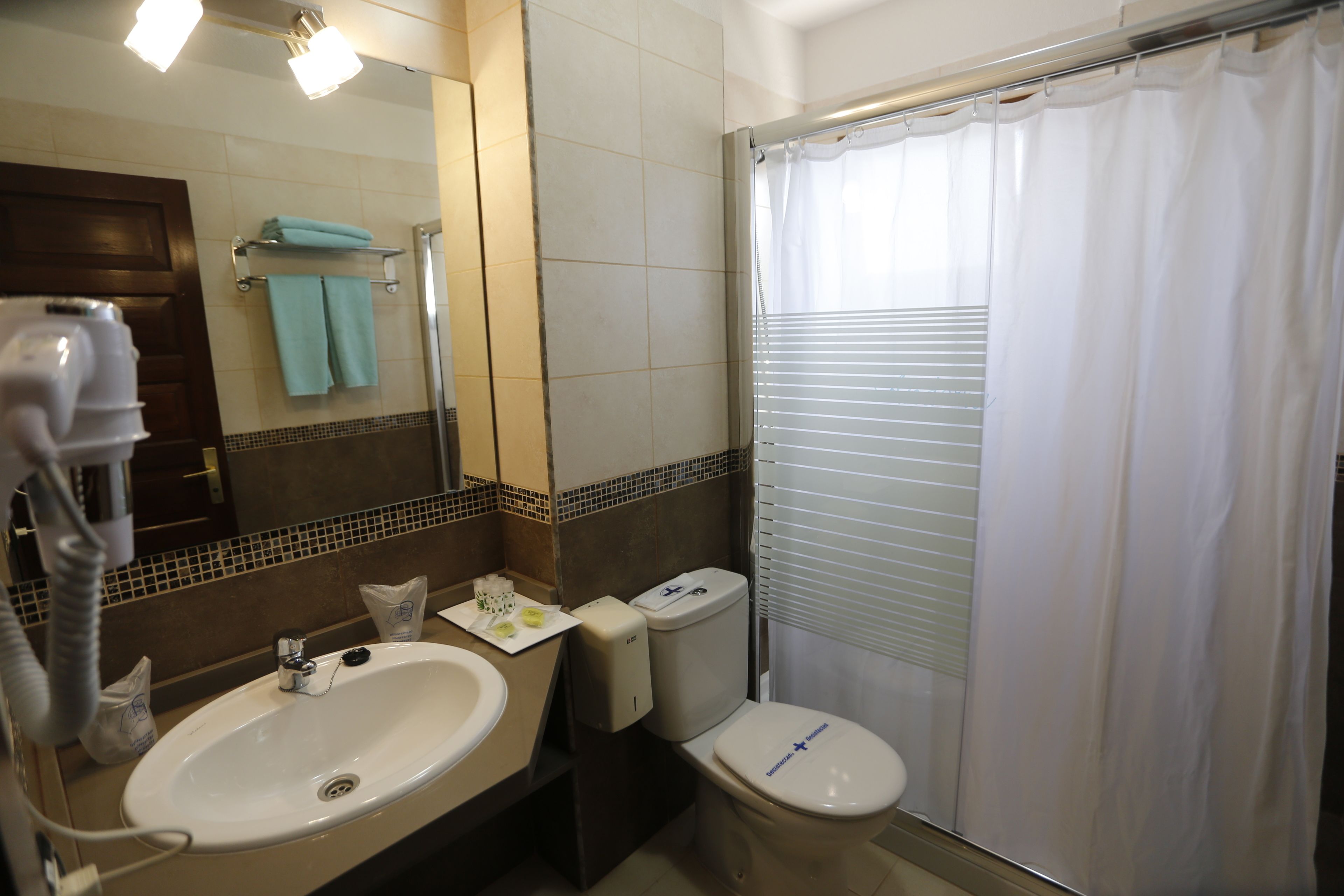 A bathroom with a sink, mirror, towel rack, toilet, and shower curtain.
