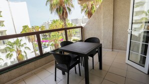 Ein Balkon mit Tisch und Stühlen, Blick auf Palmen und Gebäude, sowie eine Glastür.