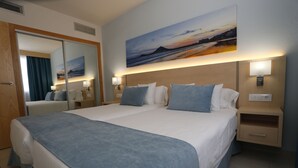 Ein Hotelzimmer mit einem großen Bett, einem Nachttisch mit Lampe, einem Spiegel und einem Bild an der Wand.