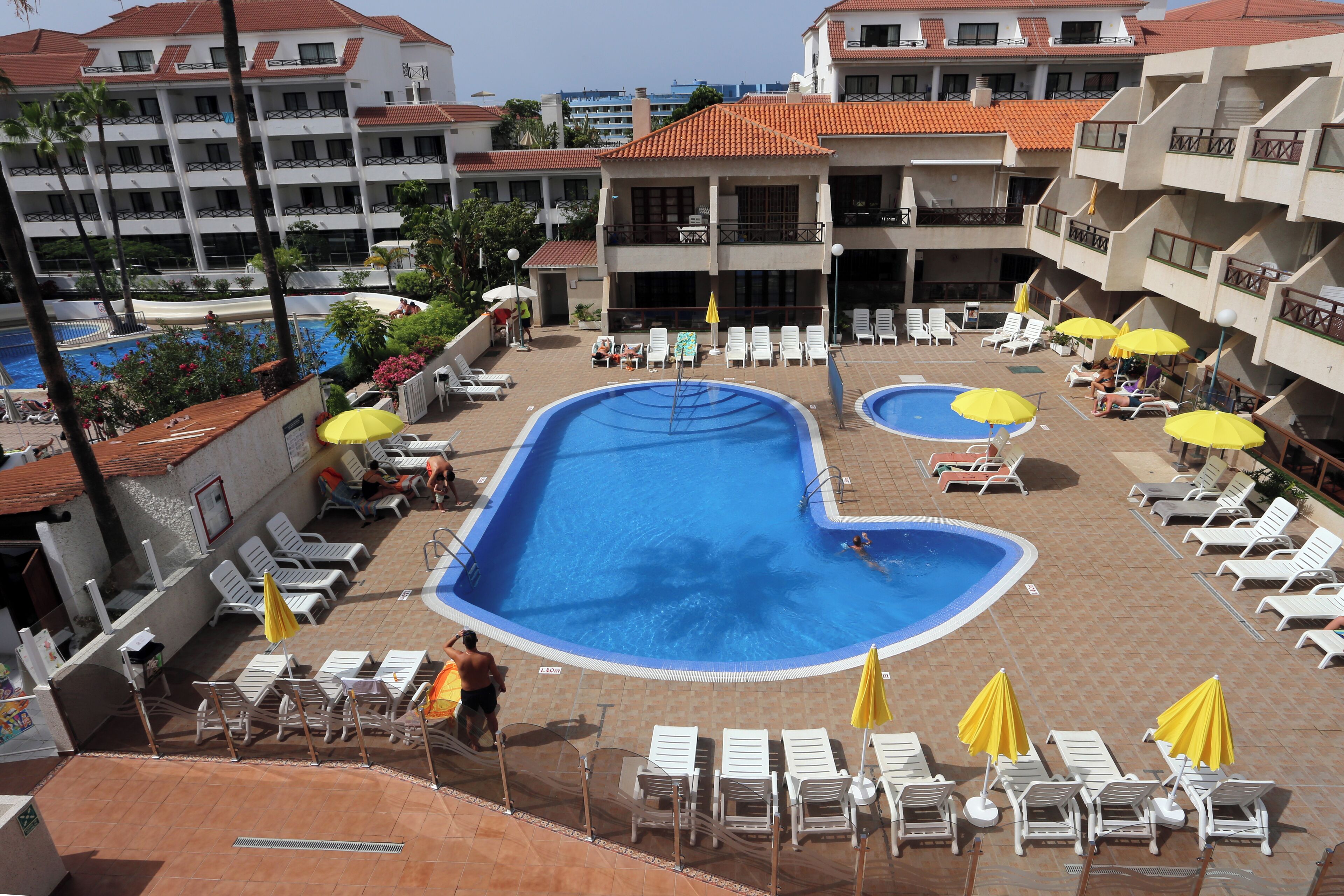 A hotel pool area with multiple pools, sun loungers, and umbrellas.