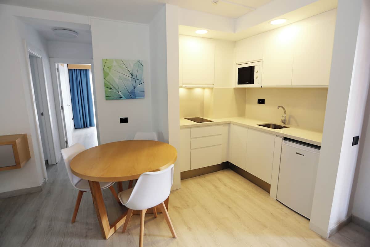 A modern kitchen with white cabinets, a wooden dining table, and a built-in microwave.