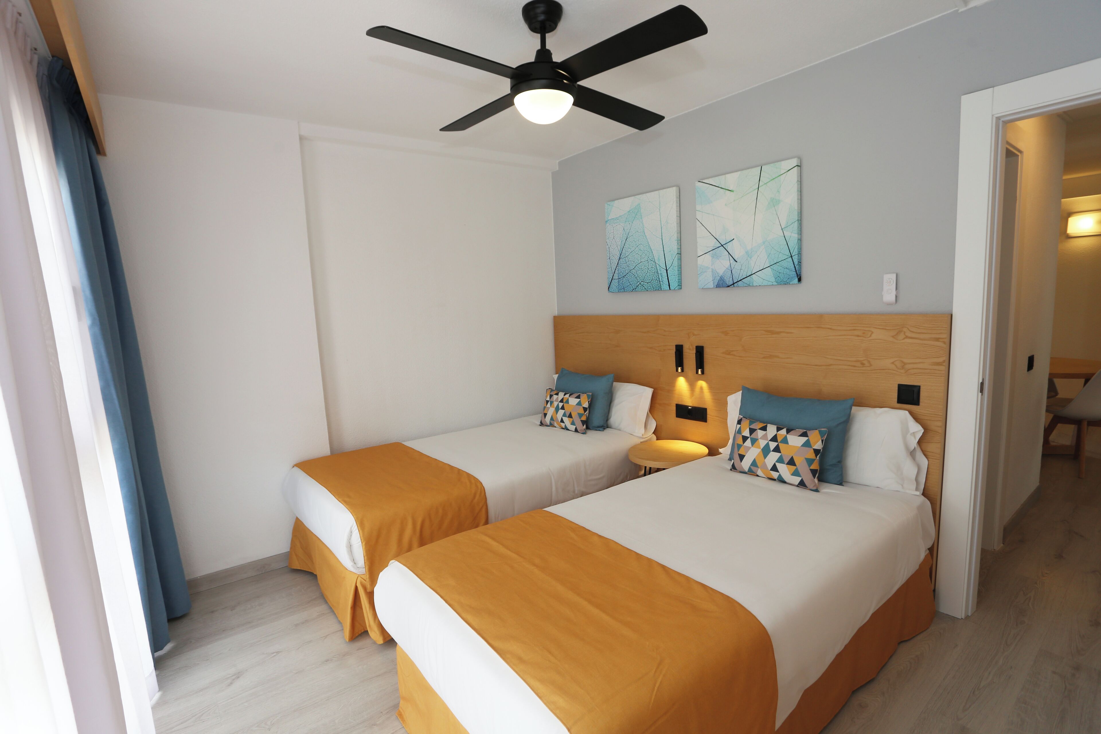 Habitación de hotel con dos camas, ventilador de techo y cuadros en la pared.