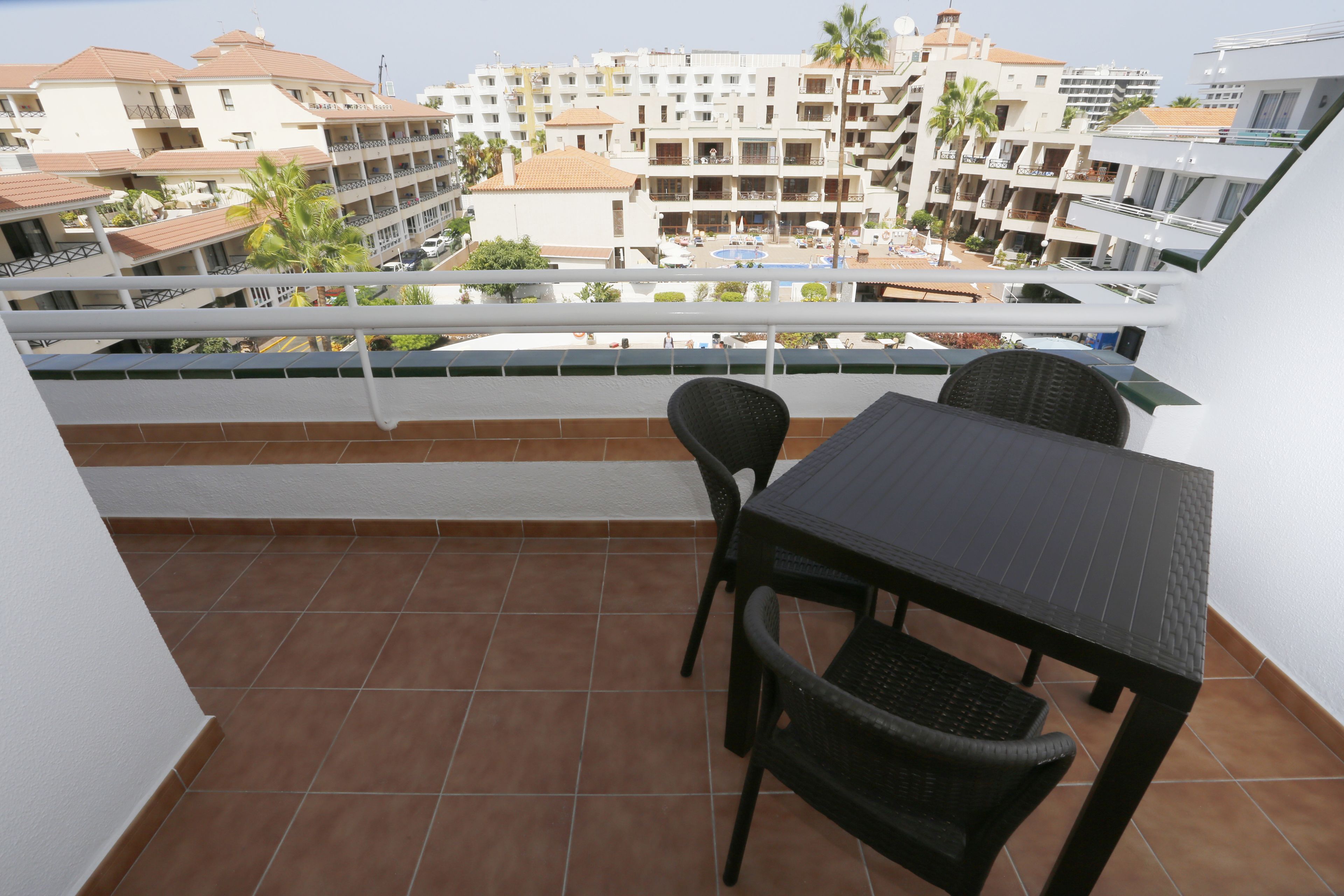 Un balcón con una mesa y sillas, con vistas a una piscina y edificios.