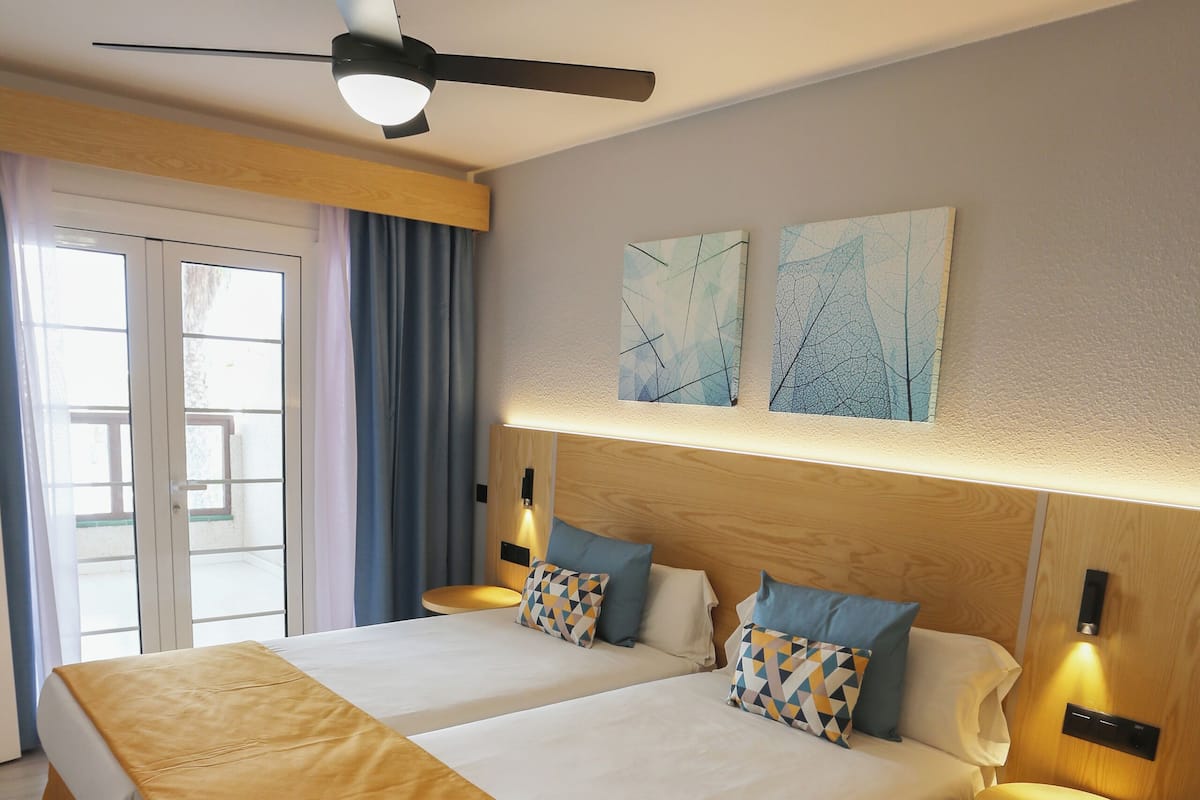 A double bed with a wooden headboard, two bedside tables with lamps, and a ceiling fan.