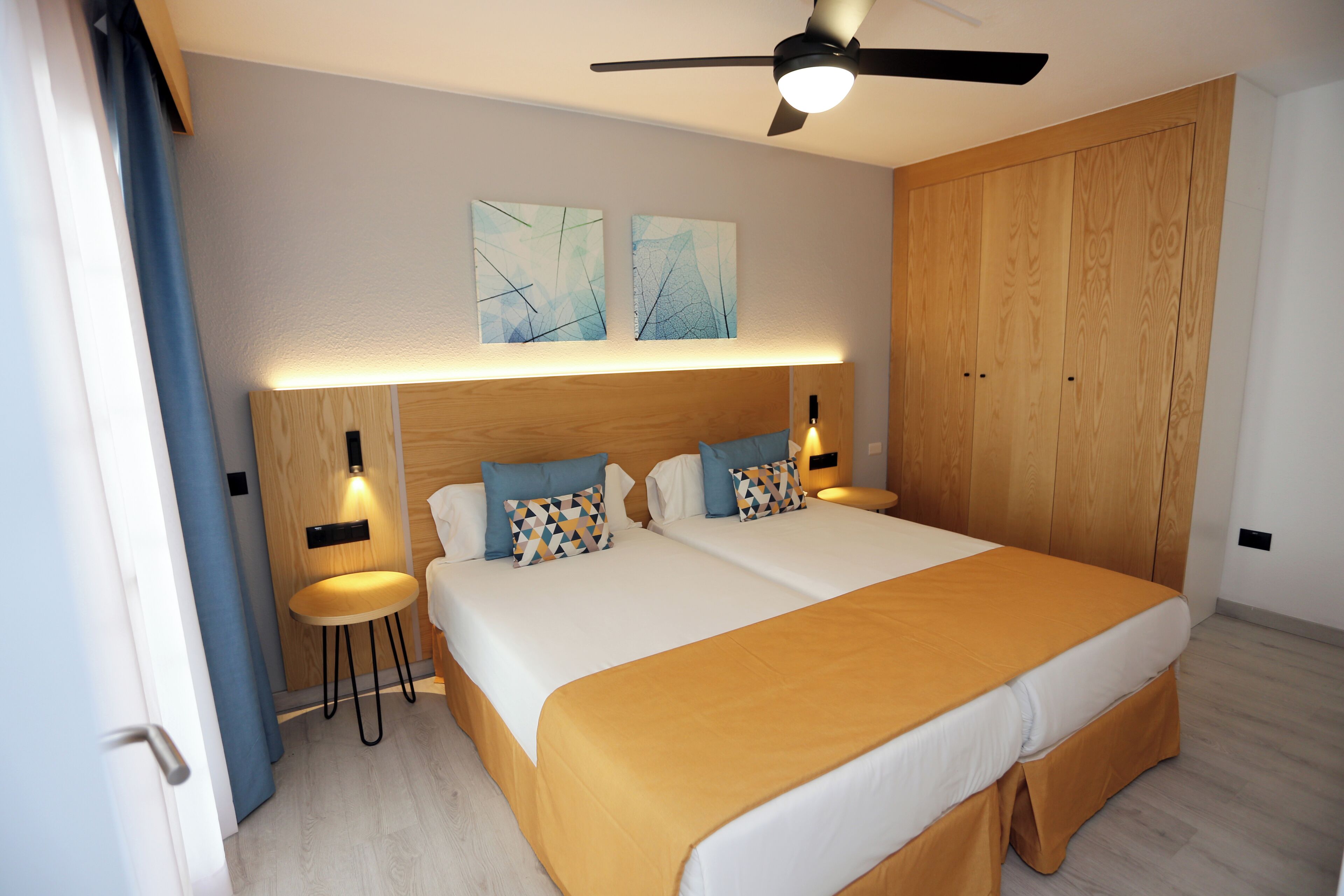 A bedroom with two beds, a ceiling fan, and wooden wardrobes.