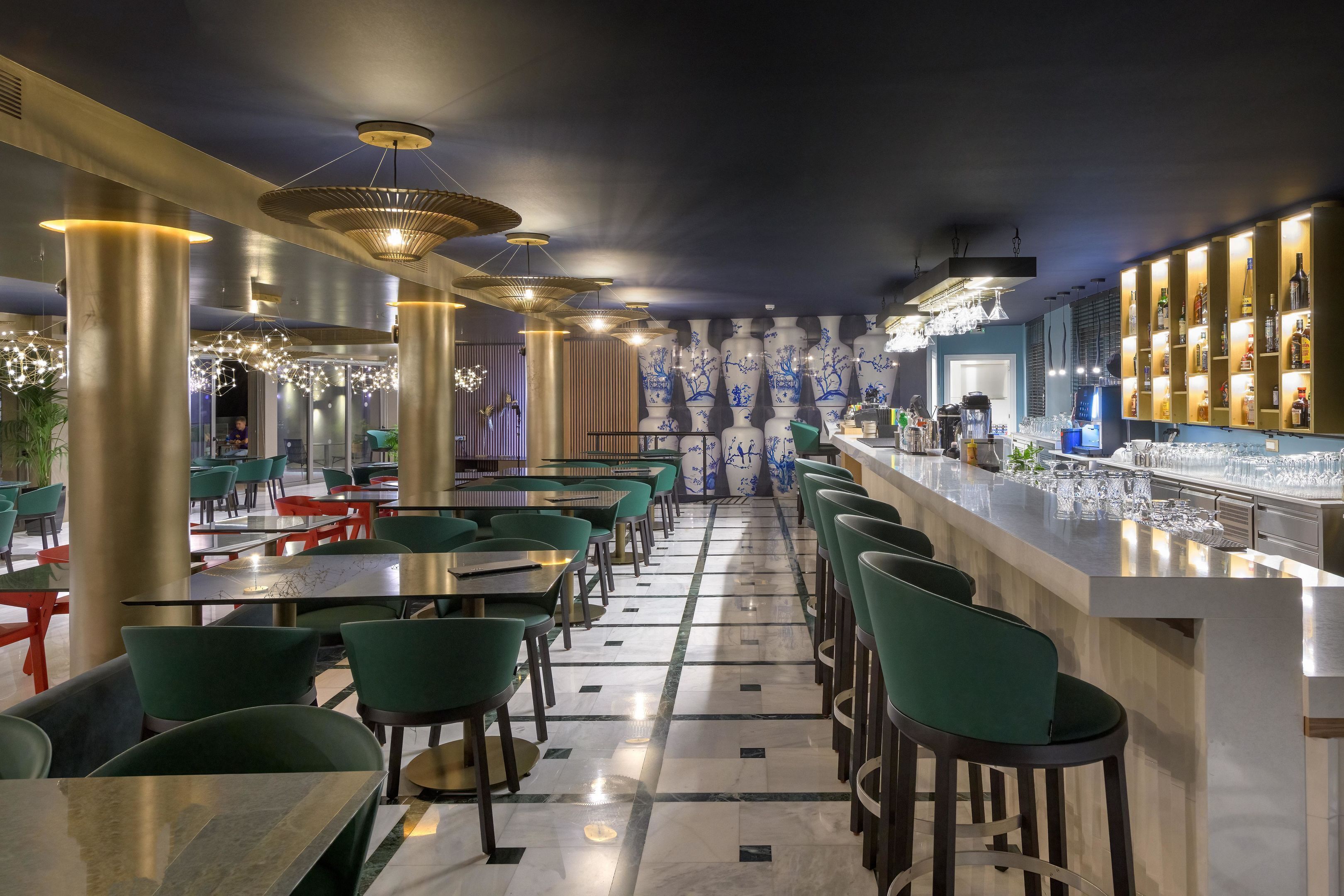 Zona de bar moderna amb cadires verdes, una barra llarga i vasetes decoratives.