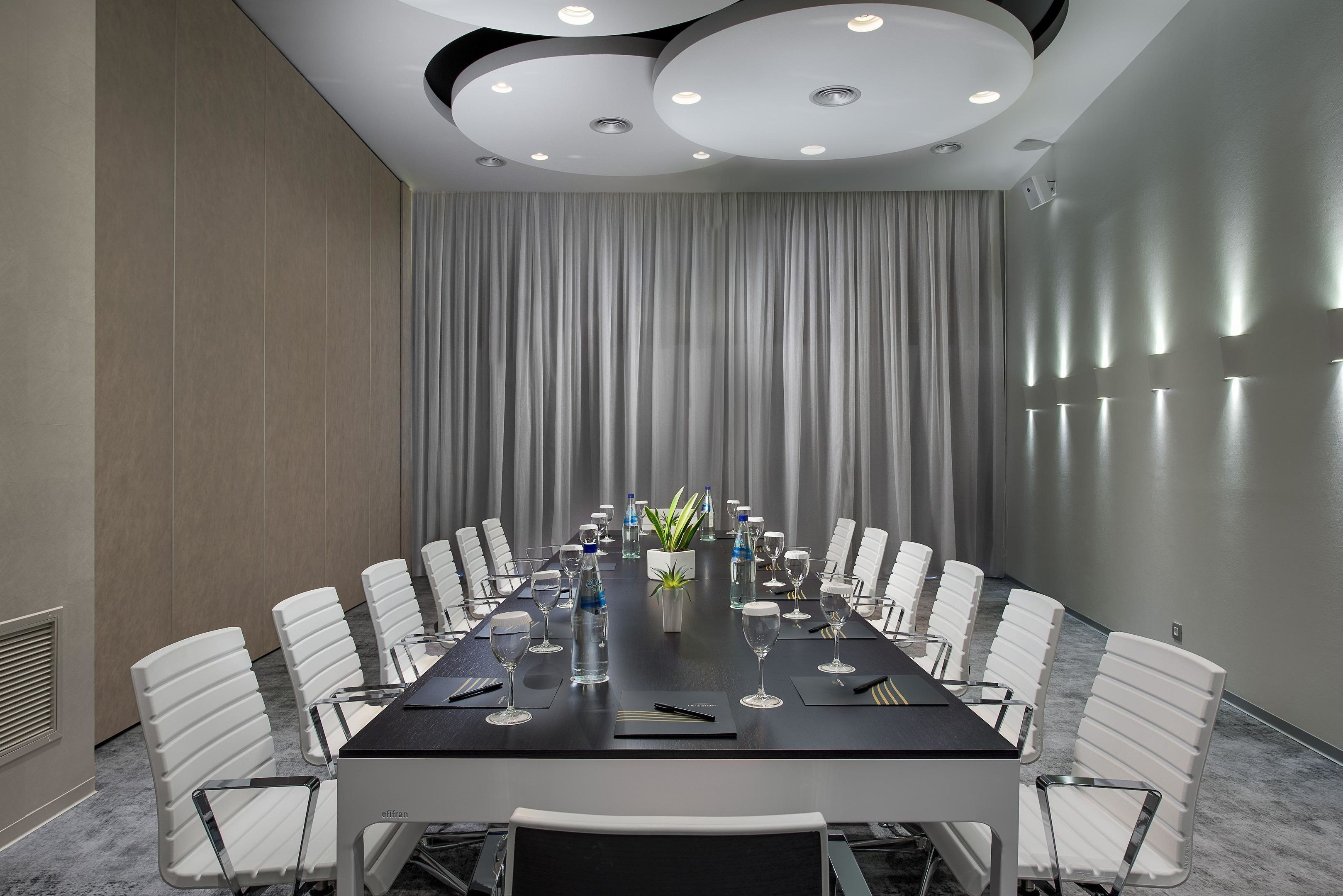 A conference room with a long table, white chairs, and a curtain backdrop.