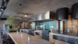 Un restaurant moderne avec une longue table en bois, des chaises noires et un luminaire suspendu au centre.