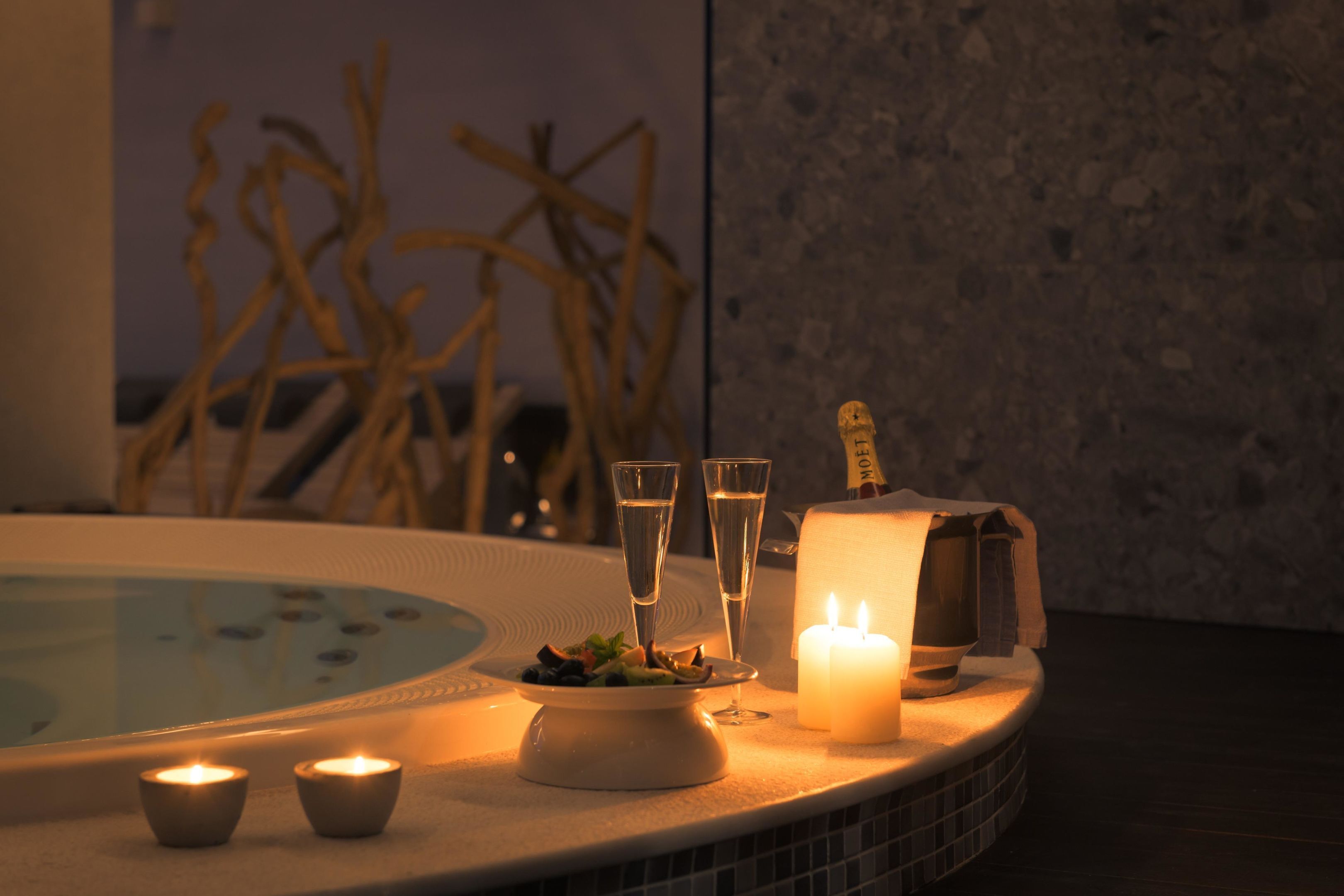 A hot tub area with candles, a plate of food, and a towel on a tiled surface.