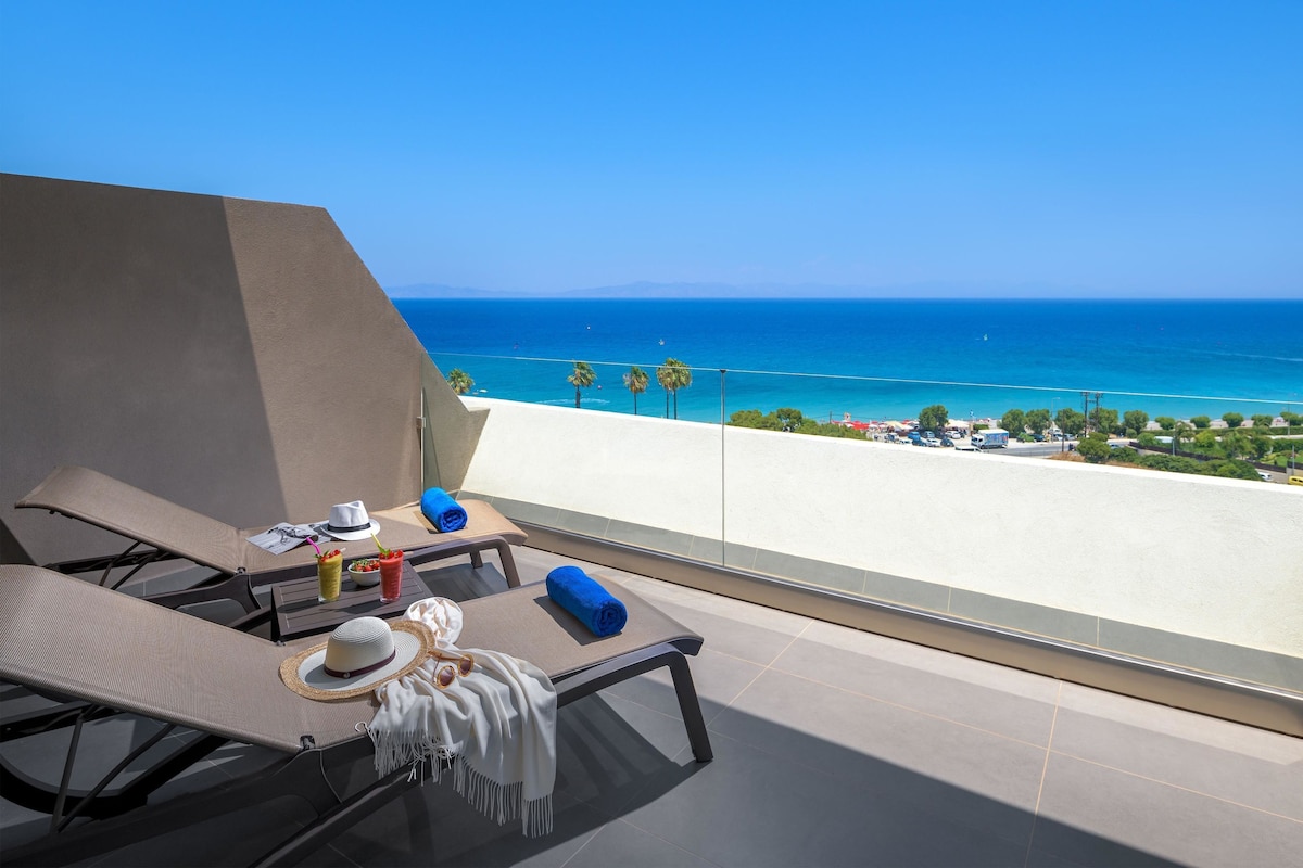 A balcony with two lounge chairs, a table with a hat, a drink, and a towel.