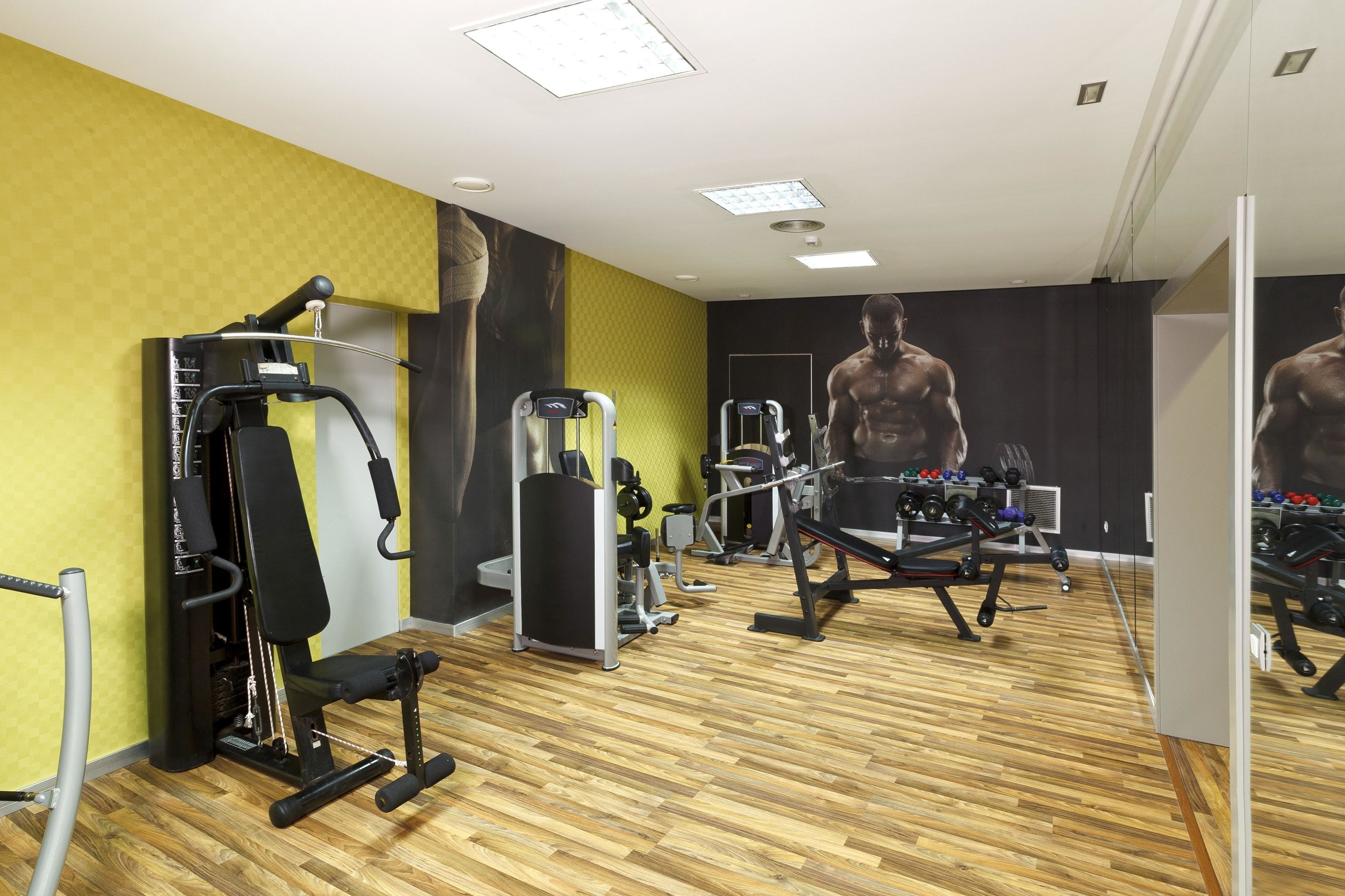 Un gimnasio con equipo de ejercicio diverso, suelo de madera y un espejo grande.