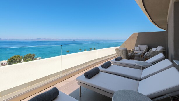 Un balcon avec des chaises longues, une petite table et une vue sur l’océan.