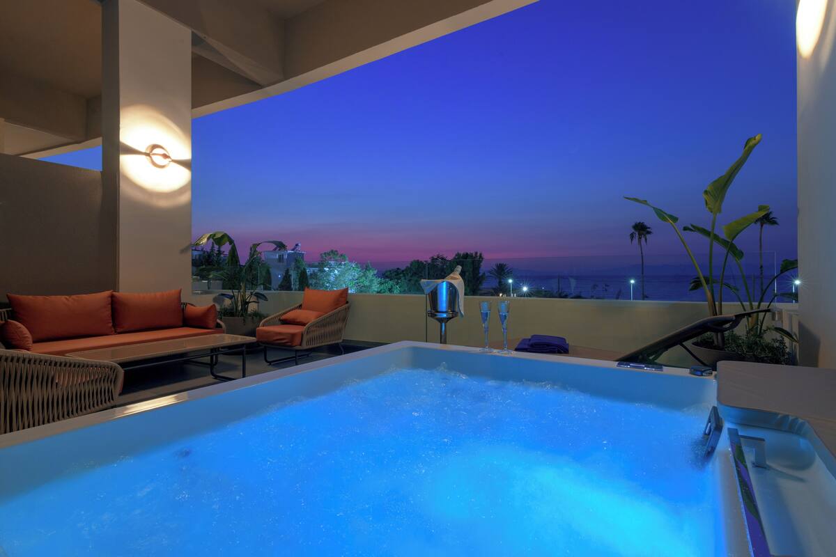 A rooftop pool area with a hot tub, orange seating, and a view of the sunset.